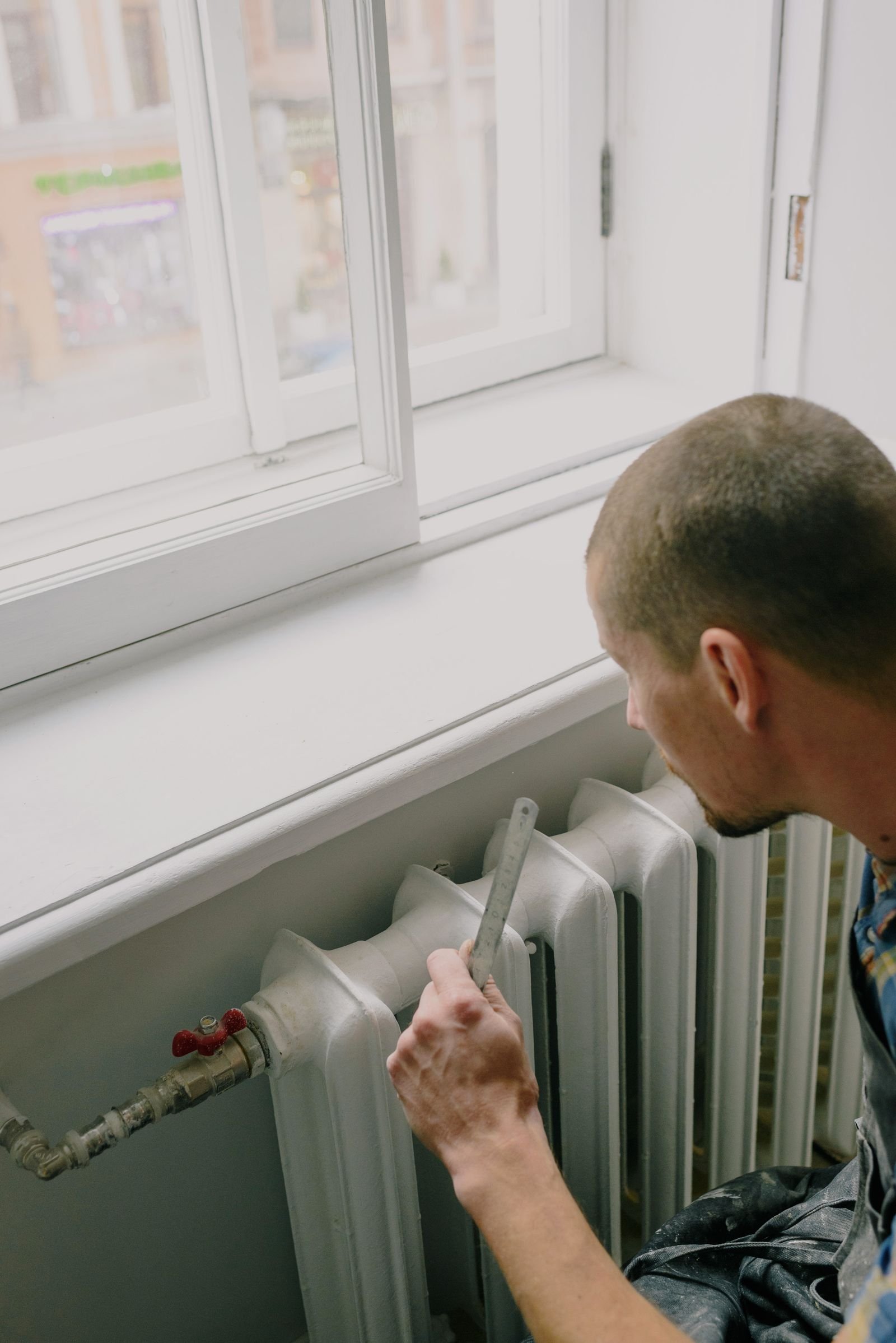 Heating engineer measuring and fitting a radiator under a window in a home
